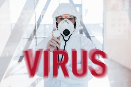 Red virus word. Nurse in protective uniform, mask and glasses standing indoorsの写真素材