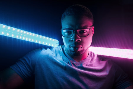Holds lighting equipment. Futuristic neon lighting. Young african american man in the studioの写真素材