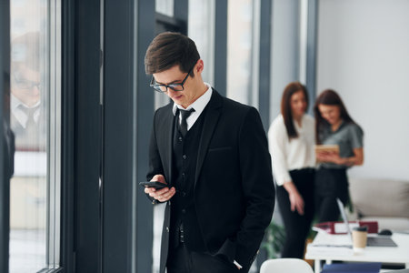 Young man with phone. Group of people in official formal clothes that is indoors in the officeの写真素材