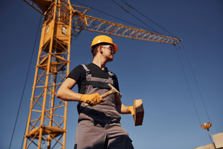 Holds brick and tool in hands. Construction worker in uniform and safety equipment have job on buildingの写真素材