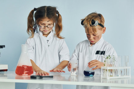 Little girl and boy in white coats plays a scientists in lab by using equipmentの写真素材
