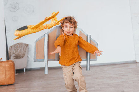 Little boy in retro pilot uniform running with toy plane indoorsの写真素材