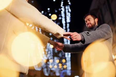 Holding each other by hands. Happy young couple celebrating New year outdoors on the streetの写真素材