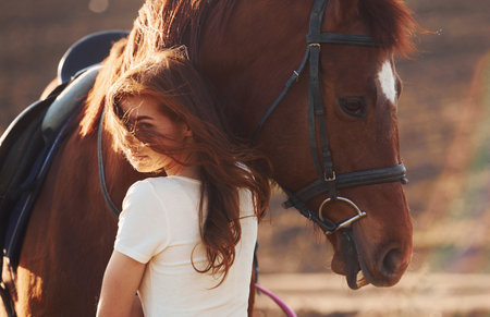 Young woman embracing her horse in agriculture field at sunny daytimeの写真素材