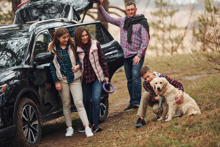 Happy family have fun with their dog near modern car outdoors in forestの写真素材