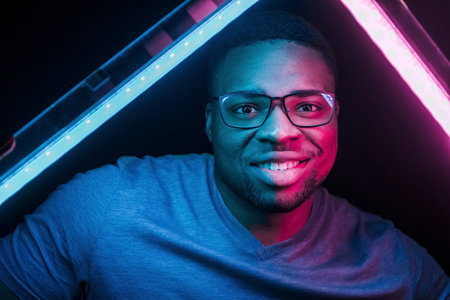 Holds lighting equipment. Futuristic neon lighting. Young african american man in the studioの写真素材