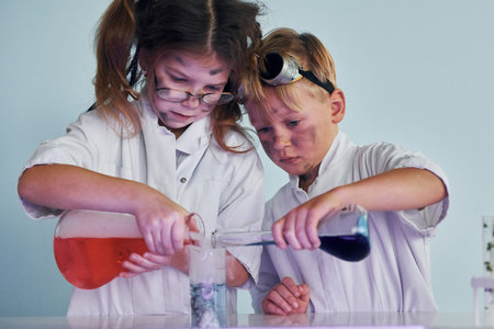 Little girl and boy in white coats plays a scientists in lab by using equipment