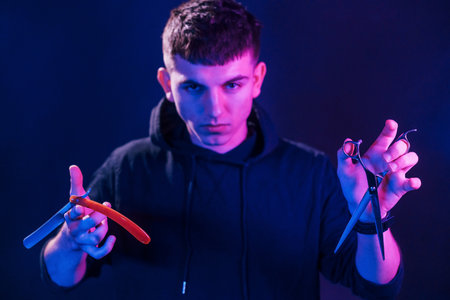 Young barber with work equipment standing in the studio with neon lightingの写真素材