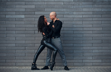 Beautiful couple in black clothes dancing together against wall outdoorsの写真素材