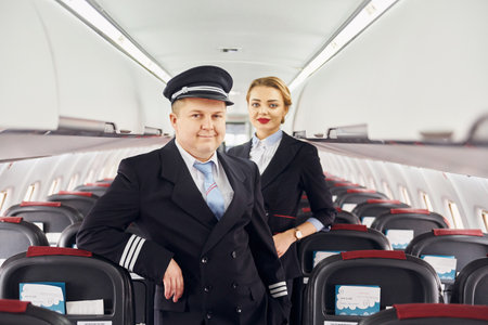Pilot in uniform and stewardess is standing inside of airplaneの写真素材
