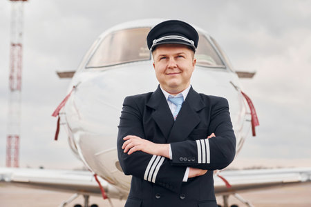 Experienced pilot in uniform standing outside near planeの写真素材