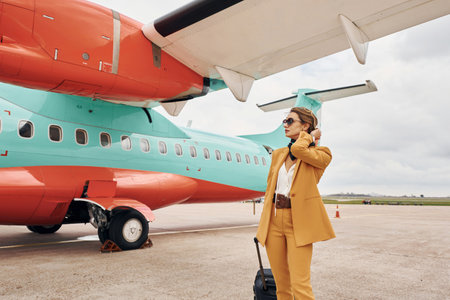 In yellow clothes. Young woman with luggage is outdoors near airplaneの写真素材