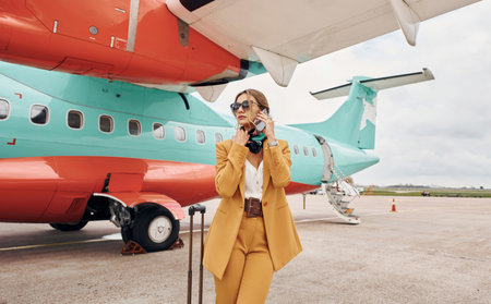 In yellow clothes. Young woman with luggage is outdoors near airplaneの写真素材