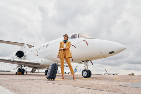 Elegant clothes. Young woman with luggage is outdoors near airplaneの写真素材