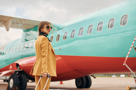Passenger woman that is in yellow clothes, sunglasses and with luggage is outdoors near planeの写真素材
