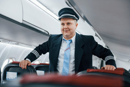 Pilot in uniform standing indoors in the passenger airplane