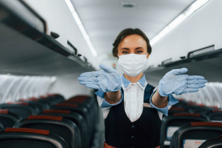 In protective gloves and mask. Young stewardess on the work in the passanger airplaneの写真素材