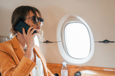 Uses phone. Young passenger woman in yellow clothes is flying in the planeの写真素材