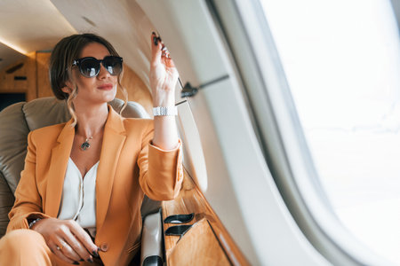 In sunglasses. Young passenger woman in yellow clothes is flying in the planeの写真素材