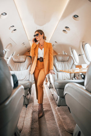 Uses phone. Young passenger woman in yellow clothes is flying in the planeの写真素材