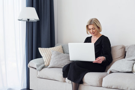 Middle-aged woman in elegant clothes is at home with laptopの写真素材