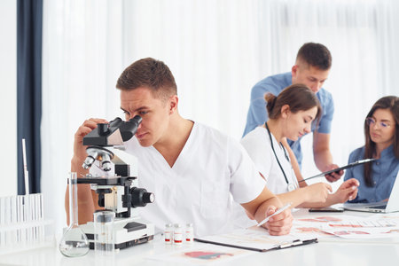 Using microscope. Group of young doctors is working together in the modern officeの写真素材