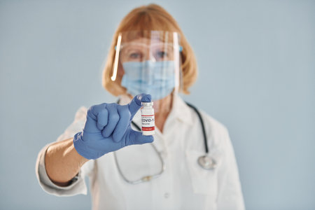Senior female doctor in white coat is standing indoors against blue backgroundの写真素材