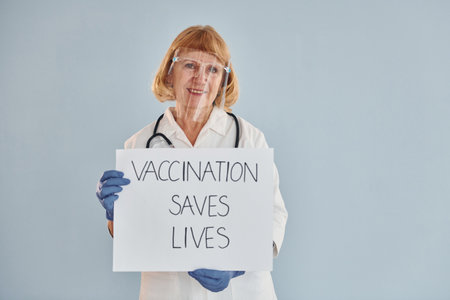 Vaccination saves lives banner. Senior female doctor in white coat is standing indoorsの写真素材