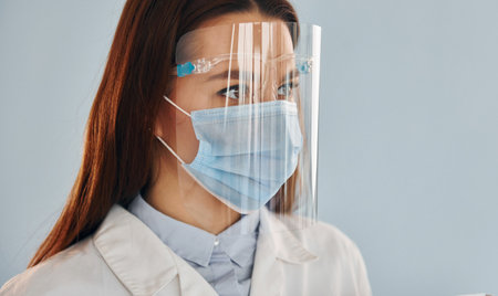 Young female doctor in white coat is standing indoors against blue backgroundの写真素材