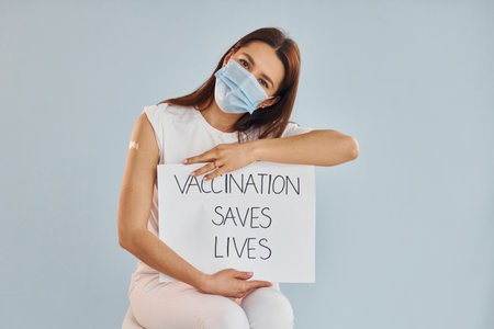Young woman in mask is sits after vaccine injection indoorsの写真素材