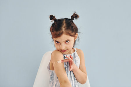 Cute little girl sits after vaccine injection indoors in hospitalの写真素材