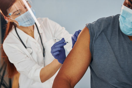 Female doctor giving injection to african american man at hospitalの写真素材