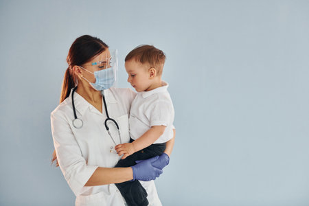 Young nurse in white coat and with stethoscope holds little boy in handsの写真素材