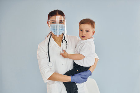 Young nurse in white coat and with stethoscope holds little boy in handsの写真素材