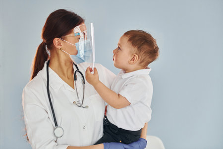 Young nurse in white coat and with stethoscope holds little boy in handsの写真素材