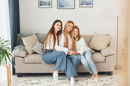 Sitting on the sofa. Young mother with her two daughters at home at daytimeの写真素材