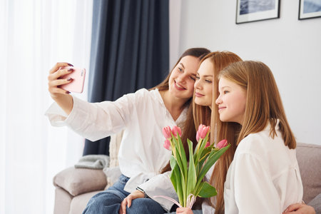 Making selfie. Young mother with her two daughters at home at daytimeの写真素材