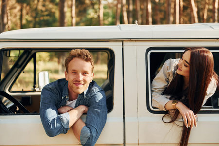 Sitting in the car. Young couple is traveling in the forest at daytime together