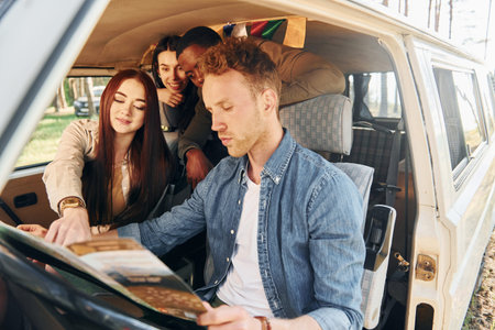 Sitting in the car. Group of young people is traveling together in the forest at daytime