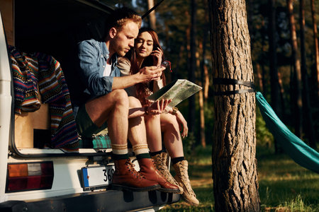 Sitting on the back of the car. Young couple is traveling in the forest at daytime togetherの写真素材