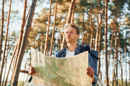 Uses map. Man is traveling alone in the forest at daytime at summer