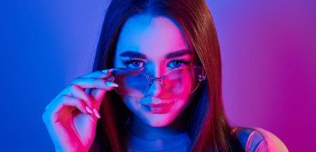 Neutral facial expression. Fashionable young woman standing in the studio with neon light