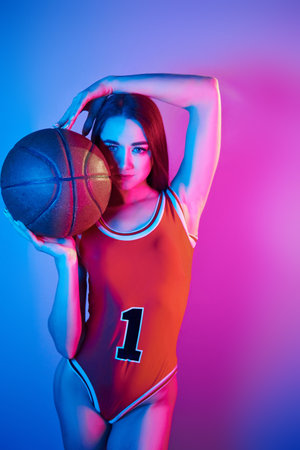 In basketball uniform. Fashionable young woman standing in the studio with neon lightの写真素材