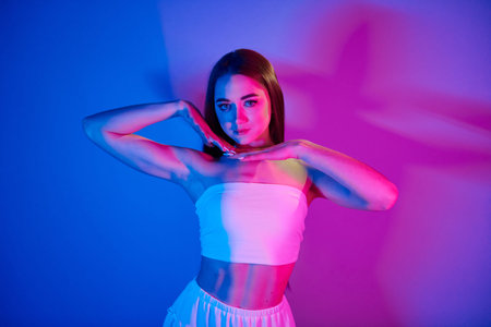 White clothes. Fashionable young woman standing in the studio with neon light