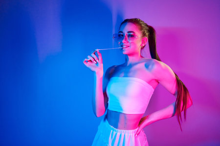 With chewing gum. Fashionable young woman standing in the studio with neon lightの写真素材