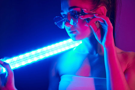 Holds neon lighting stick. Fashionable young woman standing in the studioの写真素材
