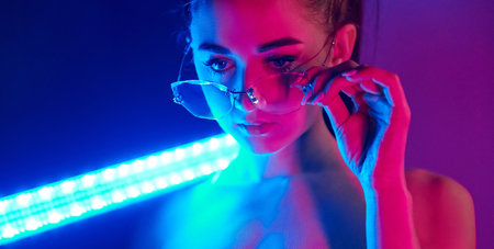 Holds neon lighting stick. Fashionable young woman standing in the studioの写真素材