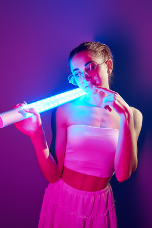 In glasses. Fashionable young woman standing in the studio with neon lightの写真素材