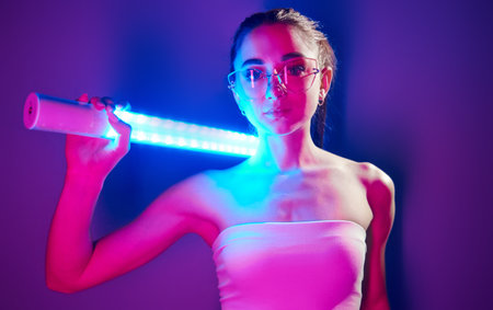 In glasses. Fashionable young woman standing in the studio with neon lightの写真素材