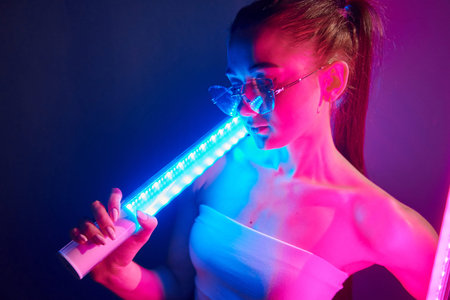 With lighting equipment. Fashionable young woman standing in the studio with neonの写真素材